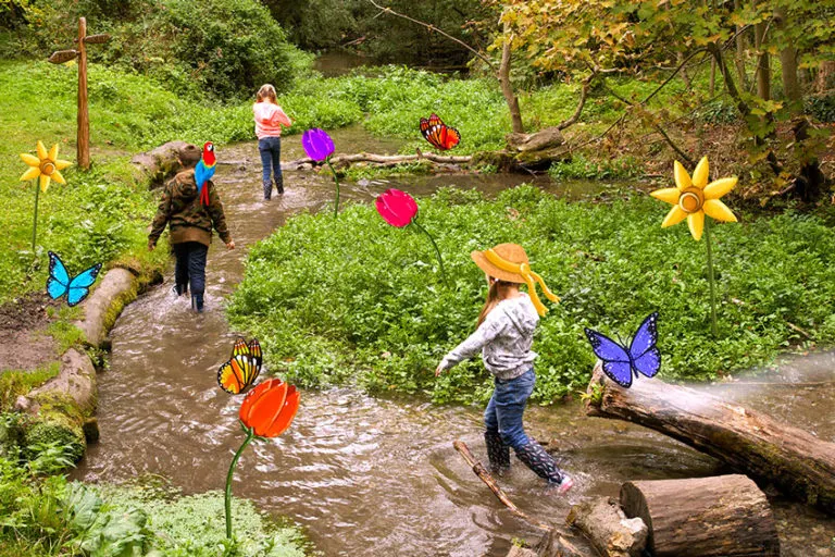 Children walking outdoors, in a stream surrounded by flowers
