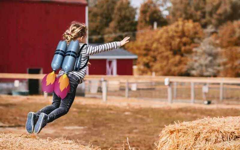 Child jumping off of a bale of hay wearing a recycled bottle jet pack